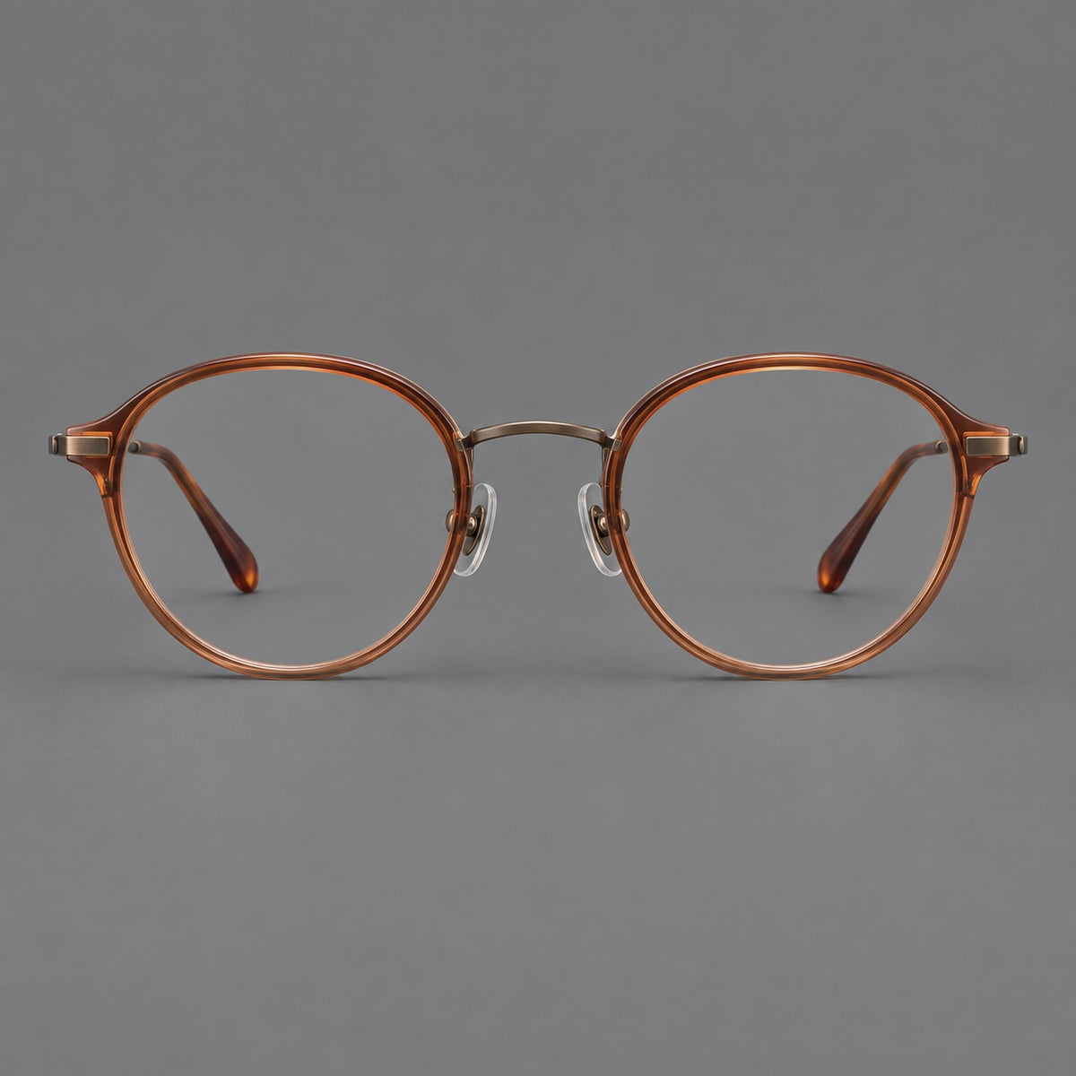 Softly rounded eyeglasses in acetate and titanium with a curved bridge and engraved temples in Tea Brown / Antique Bronze, front view