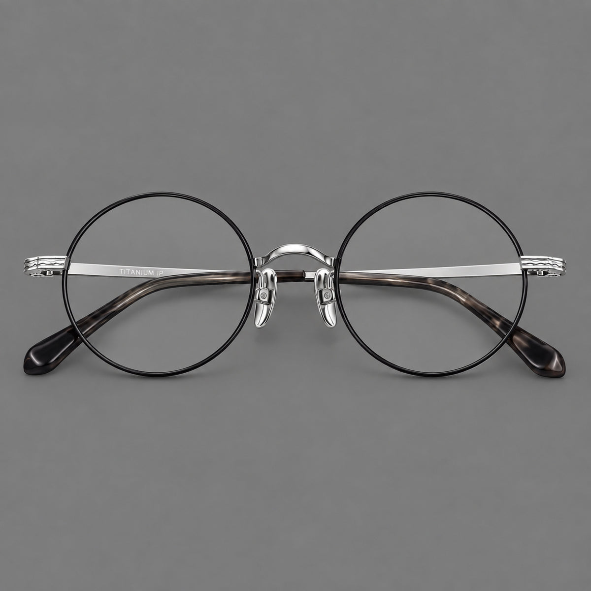 Compact circular titanium glasses with a curved bridge and wavy engraved temples in Black and Silver, front view