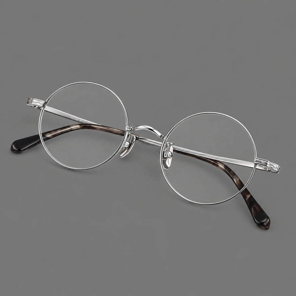 Compact circular titanium glasses with a curved bridge and wavy engraved temples in Silver, three quarter view