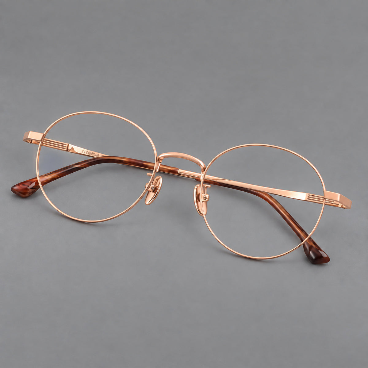 Classic circular titanium glasses with a raised bridge and lined temple accents in Rose Gold, three quarter view