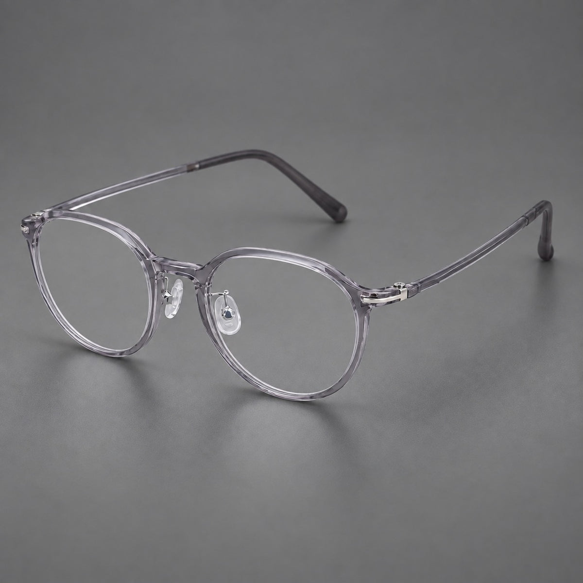 Compact round plastic eyeglasses with gently lifted corners and clear nose pads in Clear Grey, three quarter view