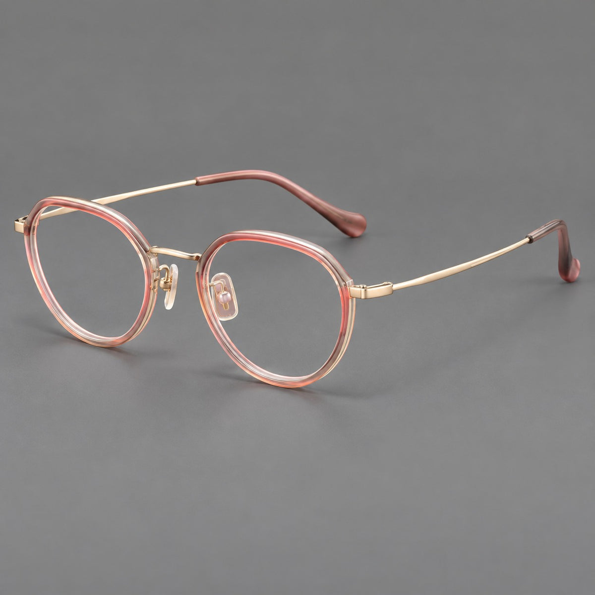 Rounded eyeglasses in acetate and titanium with gently arched brows and engraved metal temples in Amber Pink / Gold, three quarter view
