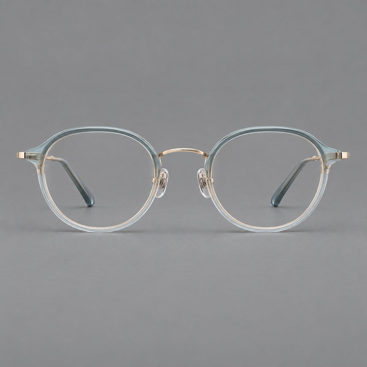 Softly rounded eyeglasses in acetate and titanium with a curved bridge and engraved temples in Ice Blue Grey / Gold, front view