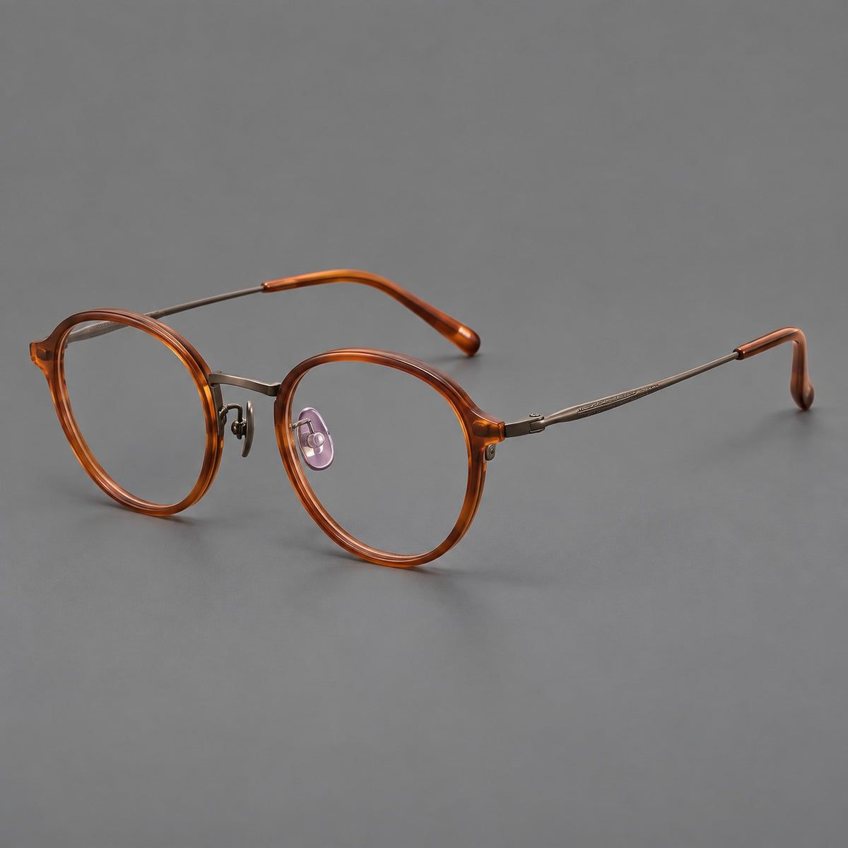 Softly rounded eyeglasses in acetate and titanium with a curved bridge and engraved temples in Tea Brown / Antique Bronze, three quarter view