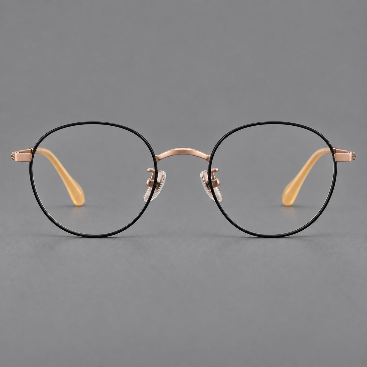 Compact round titanium glasses with an arched bridge and textured temple accents in Black and Rose Gold, front view
