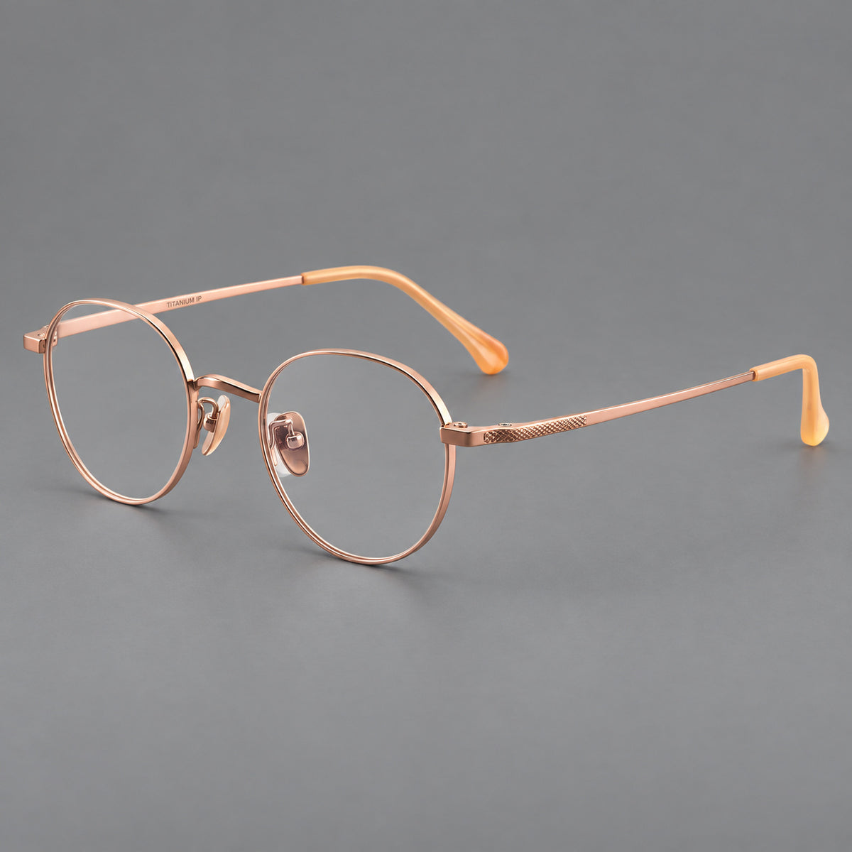 Compact round titanium glasses with an arched bridge and textured temple accents in Rose Gold, three quarter view