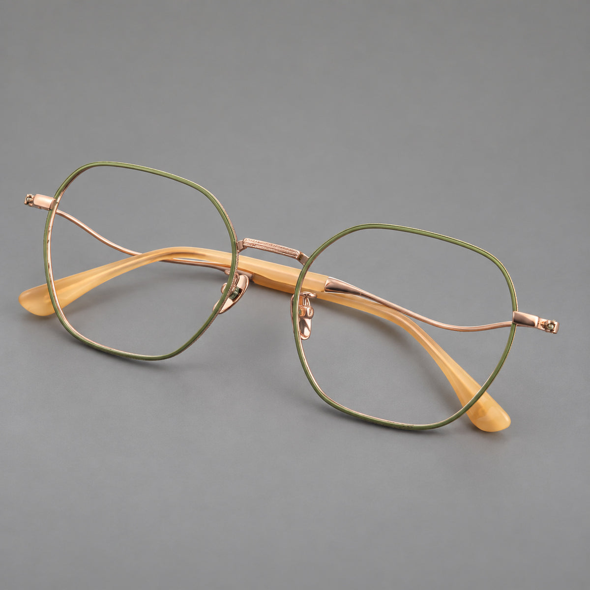 Geometric titanium glasses with engraved rim edges and curved temple joins in Green and Rose Gold, three quarter view