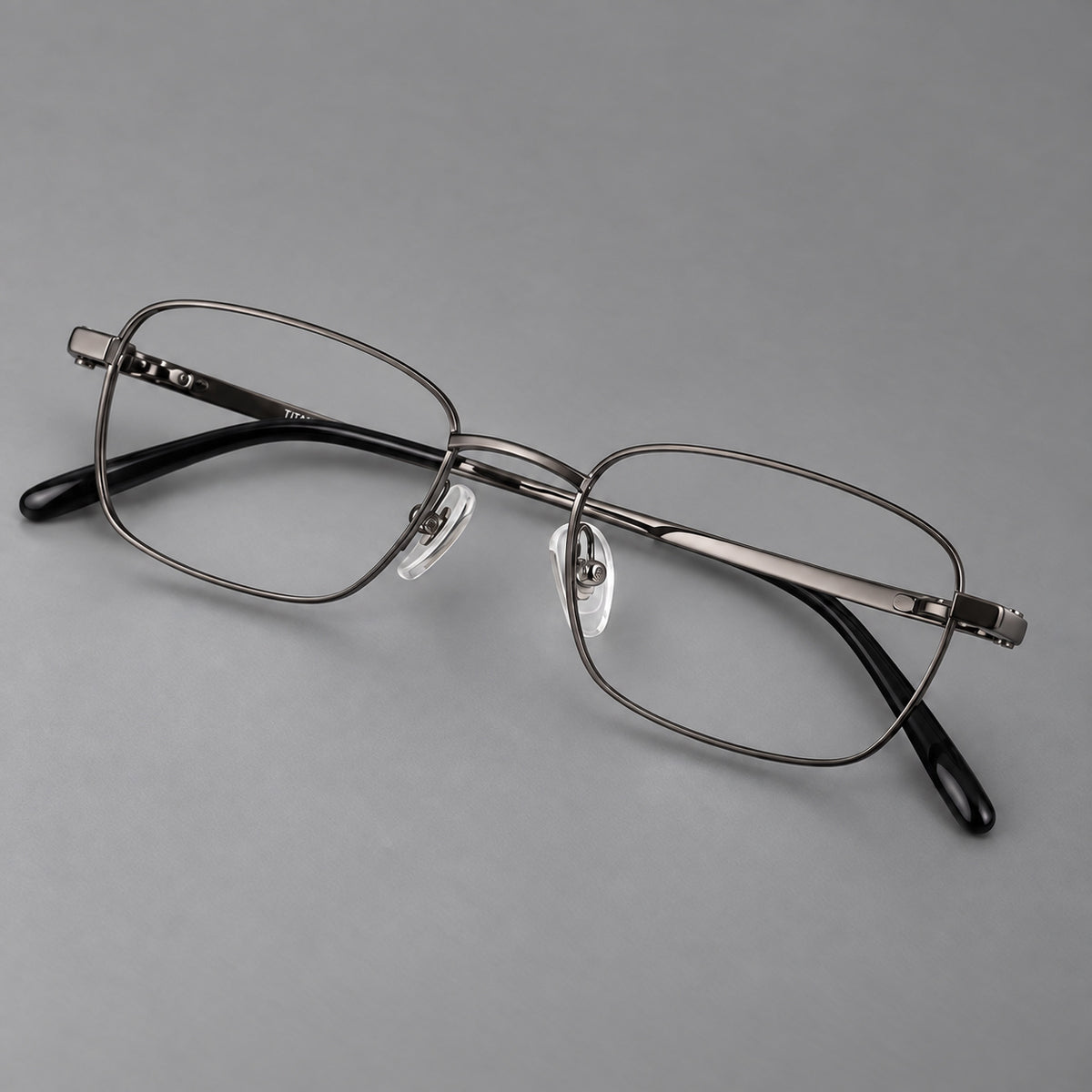 Shallow rectangular titanium glasses with a broad bridge and stepped temple joins in Gunmetal, three quarter view